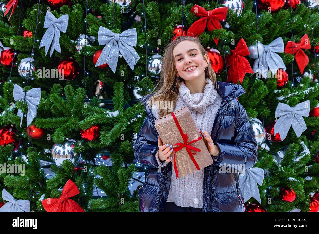 Bonne fille blonde souriante avec cadeau de Noël.Jolie fille adolescente d'origine caucasienne dans une veste en duvet tient un cadeau de Noël en h Banque D'Images