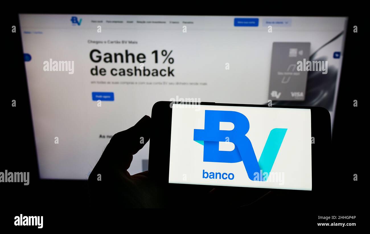 Personne tenant smartphone avec logo de la société brésilienne Banco Votorantim S.A. sur écran devant le site.Mise au point sur l'affichage du téléphone. Banque D'Images