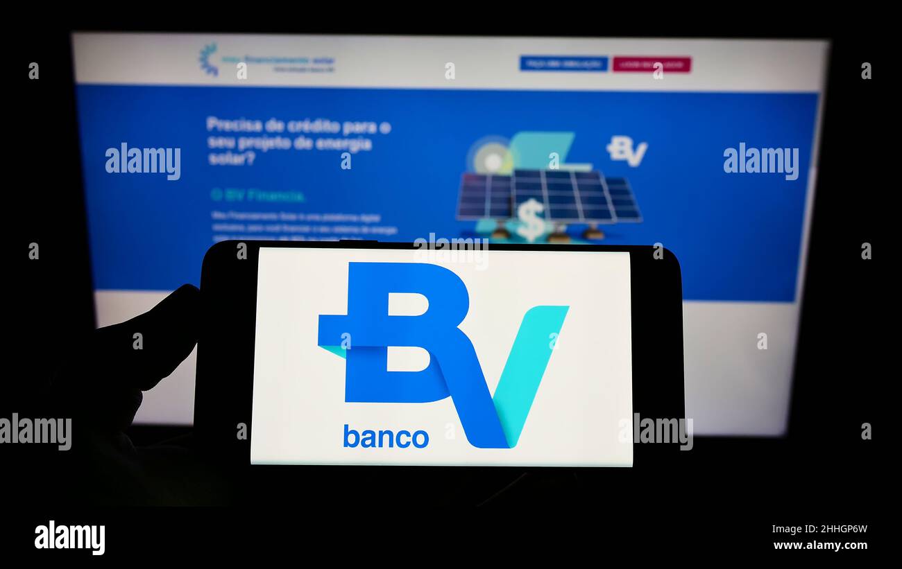 Personne tenant un téléphone portable avec le logo de la société brésilienne Banco Votorantim S.A. sur l'écran en face de la page Web d'affaires.Mise au point sur l'affichage du téléphone. Banque D'Images