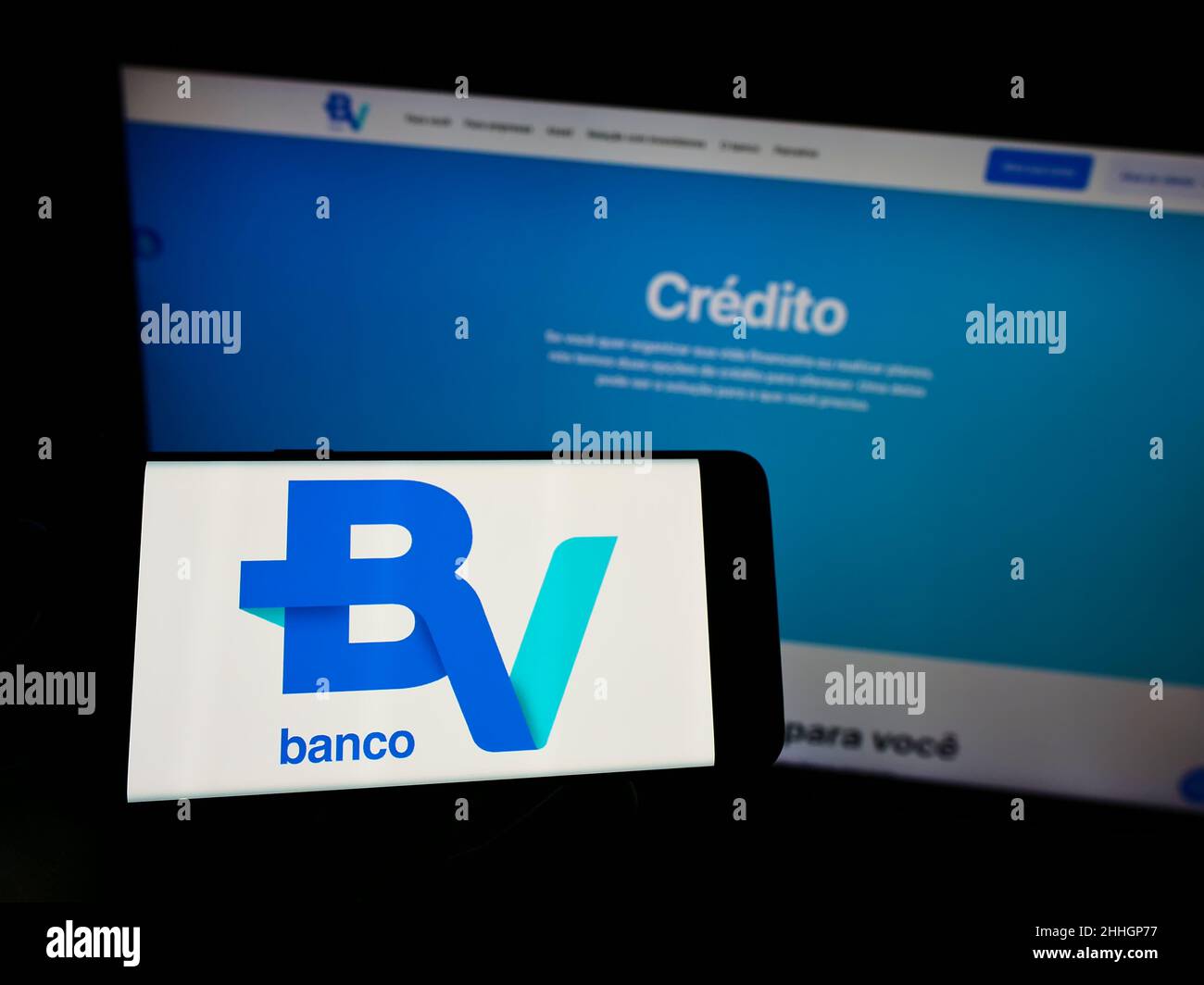Personne tenant un téléphone portable avec le logo de la société brésilienne Banco Votorantim S.A. sur écran devant la page web d'affaires.Mise au point sur l'affichage du téléphone. Banque D'Images
