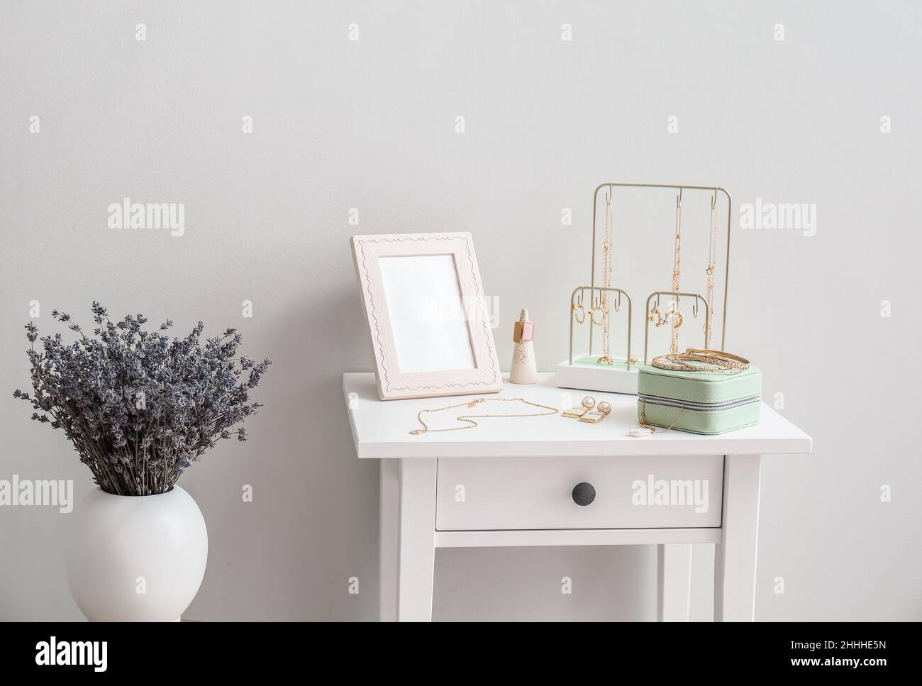 Table avec bijoux élégants et vase avec fleurs près du mur lumineux Banque D'Images