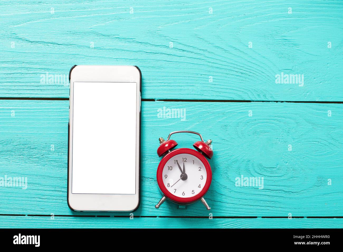 Téléphone mobile et réveil rétro rouge avec cinq minutes à douze heures sur fond bleu en bois.Vue de dessus et écran vide Banque D'Images