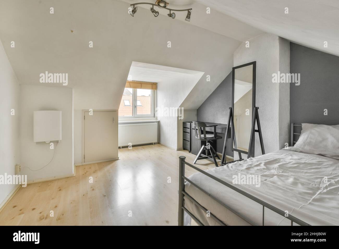 Une chambre moderne et lumineuse avec un lit double, un grand miroir et des équipements de bureau gris Banque D'Images