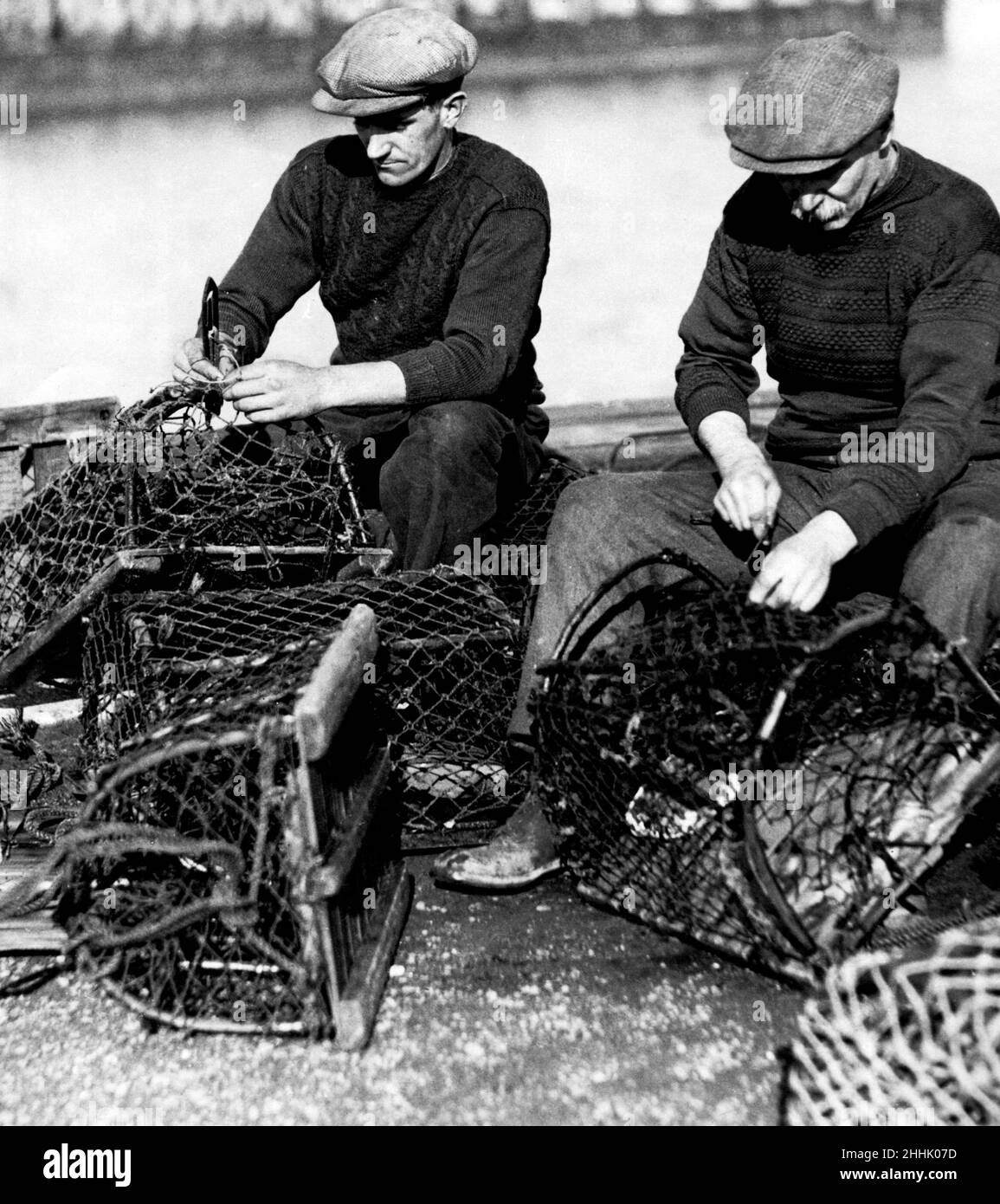 En train de faire leurs filets - flânez les pêcheurs qui réparent leurs pots de crabe sur la jetée.26th février 1932. Banque D'Images