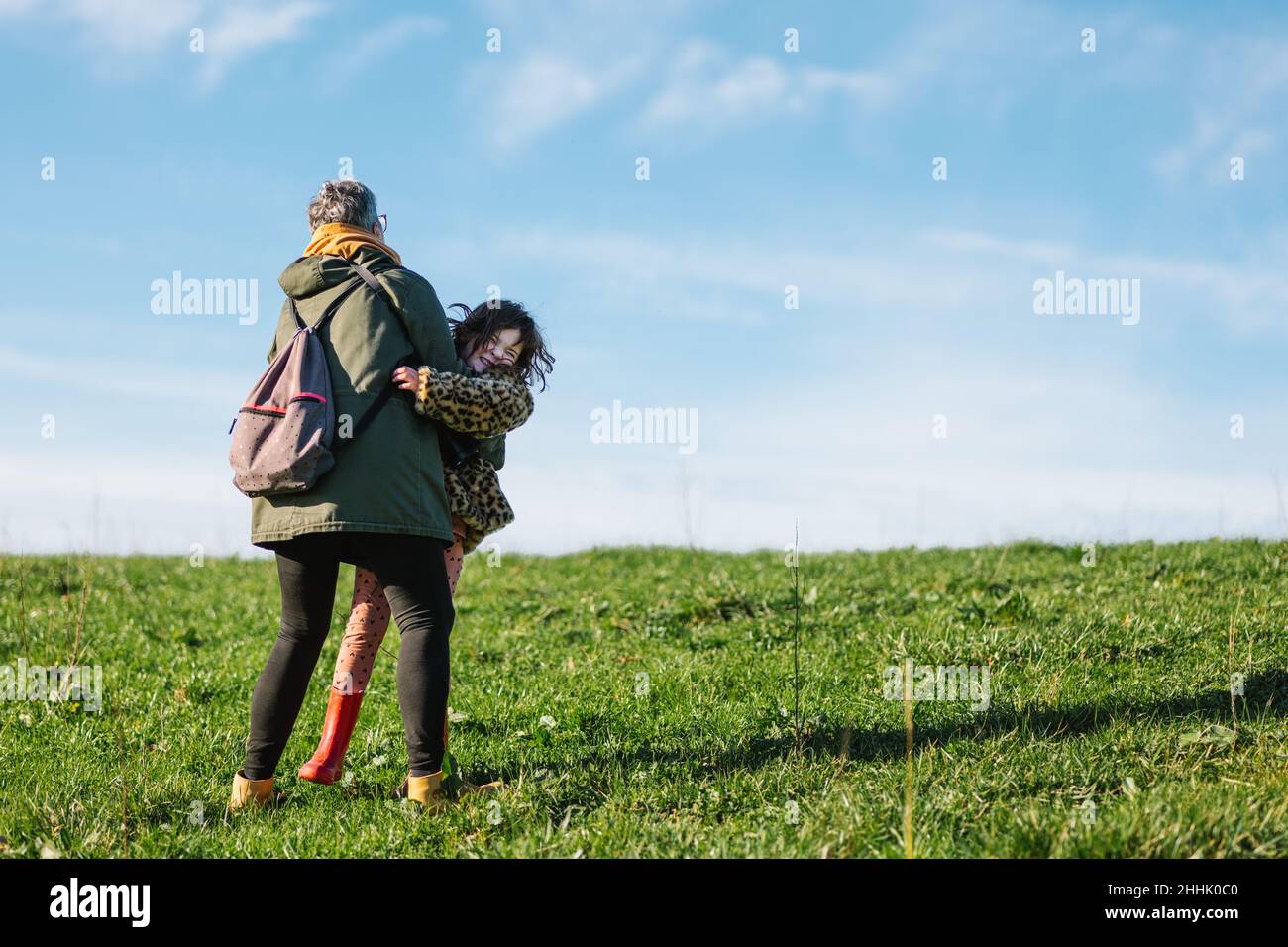 Tout le corps de grand-fille en vêtements d'extérieur embrassant la petite-fille riant avec les yeux fermés tout en s'amusant ensemble dans la nature Banque D'Images