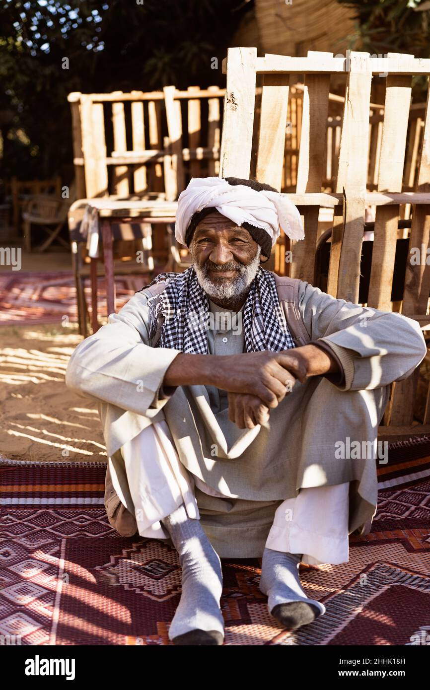 Homme nubien âgé dans une tenue ethnique assis sur un tapis dans la cour et  regardant la caméra au soleil Photo Stock - Alamy