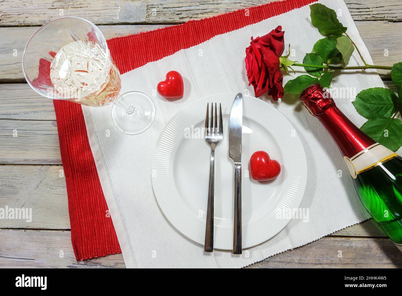 Table pour un dîner de la Saint-Valentin, rose rouge et deux coeurs, verre de chapagne et bouteille autour d'une assiette blanche sur les serviettes et sur une table rustique en bois Banque D'Images