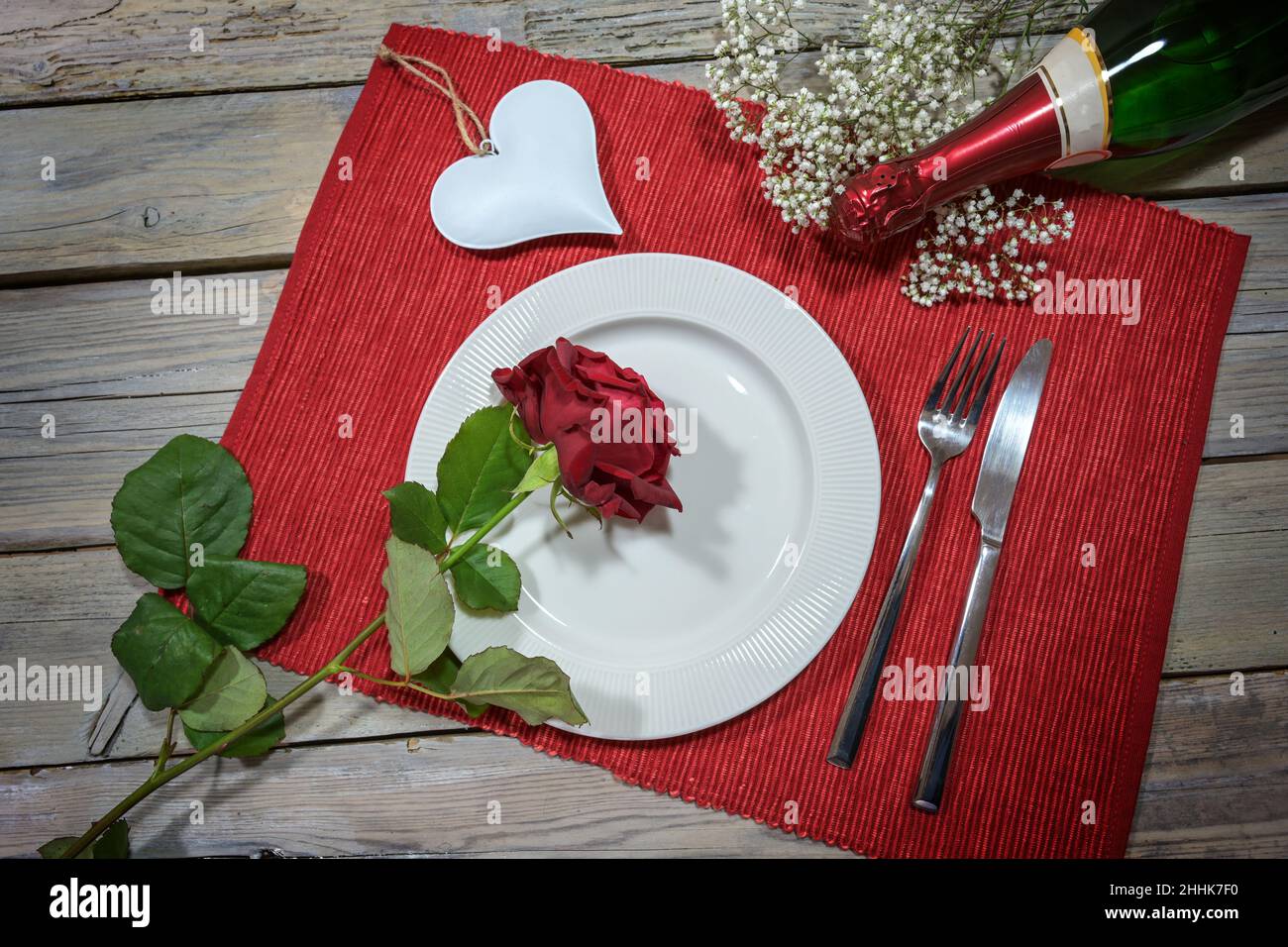 Dîner romantique de Saint Valentin, assiette blanche avec une rose rouge, en forme de coeur et une bouteille de champagne sur une serviette et une table rustique en bois, concept d'amour, h Banque D'Images