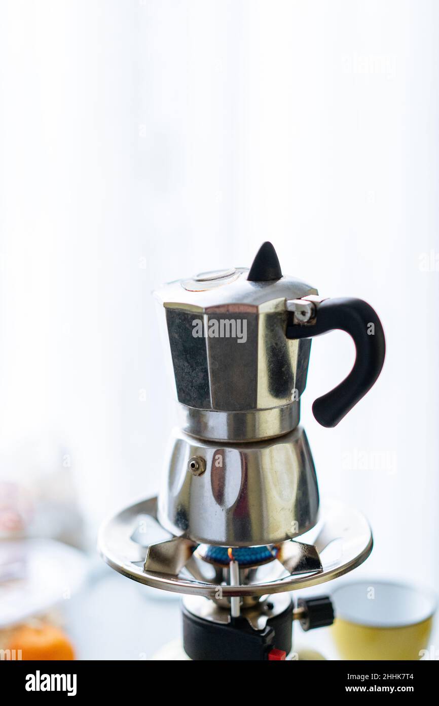 Moka moderne en métal pour préparer du café placé sur un poêle à gaz inoxydable dans une cuisine légère avec des tasses sur fond flou Banque D'Images