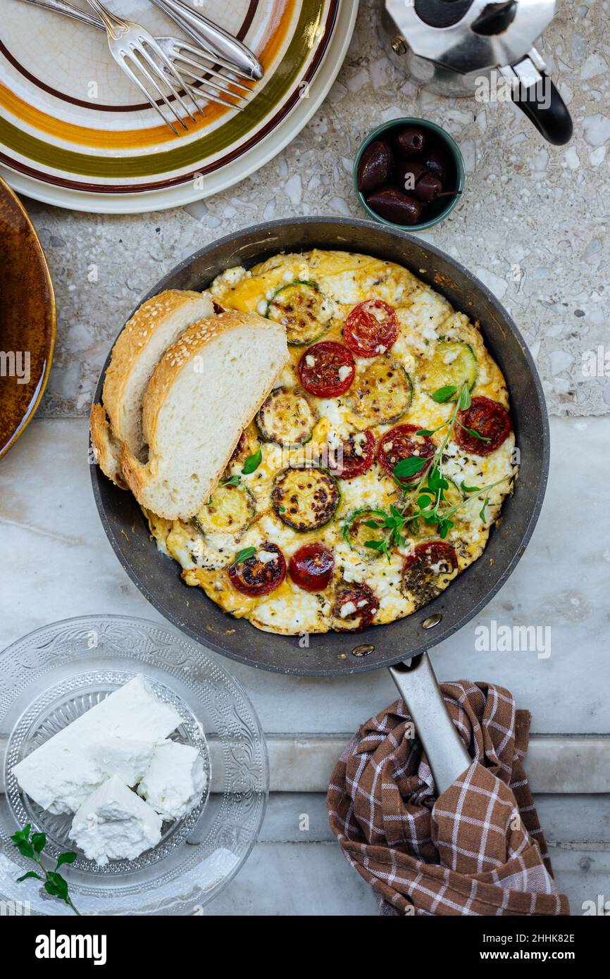 Vue de dessus de frittata grecque traditionnelle avec tomates cerises et fromage feta dans une poêle avec pain dans une cuisine légère Banque D'Images