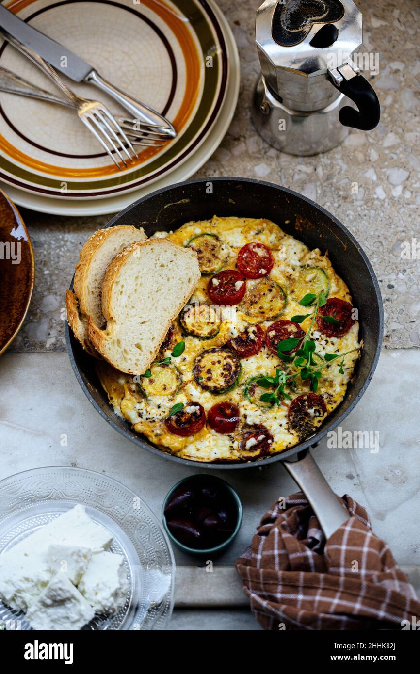 Vue de dessus de frittata grecque traditionnelle avec tomates cerises et fromage feta dans une poêle avec pain dans une cuisine légère Banque D'Images