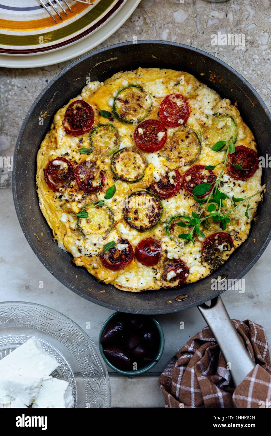 Vue de dessus de frittata grecque traditionnelle avec tomates cerises et fromage feta dans une poêle avec pain dans une cuisine légère Banque D'Images