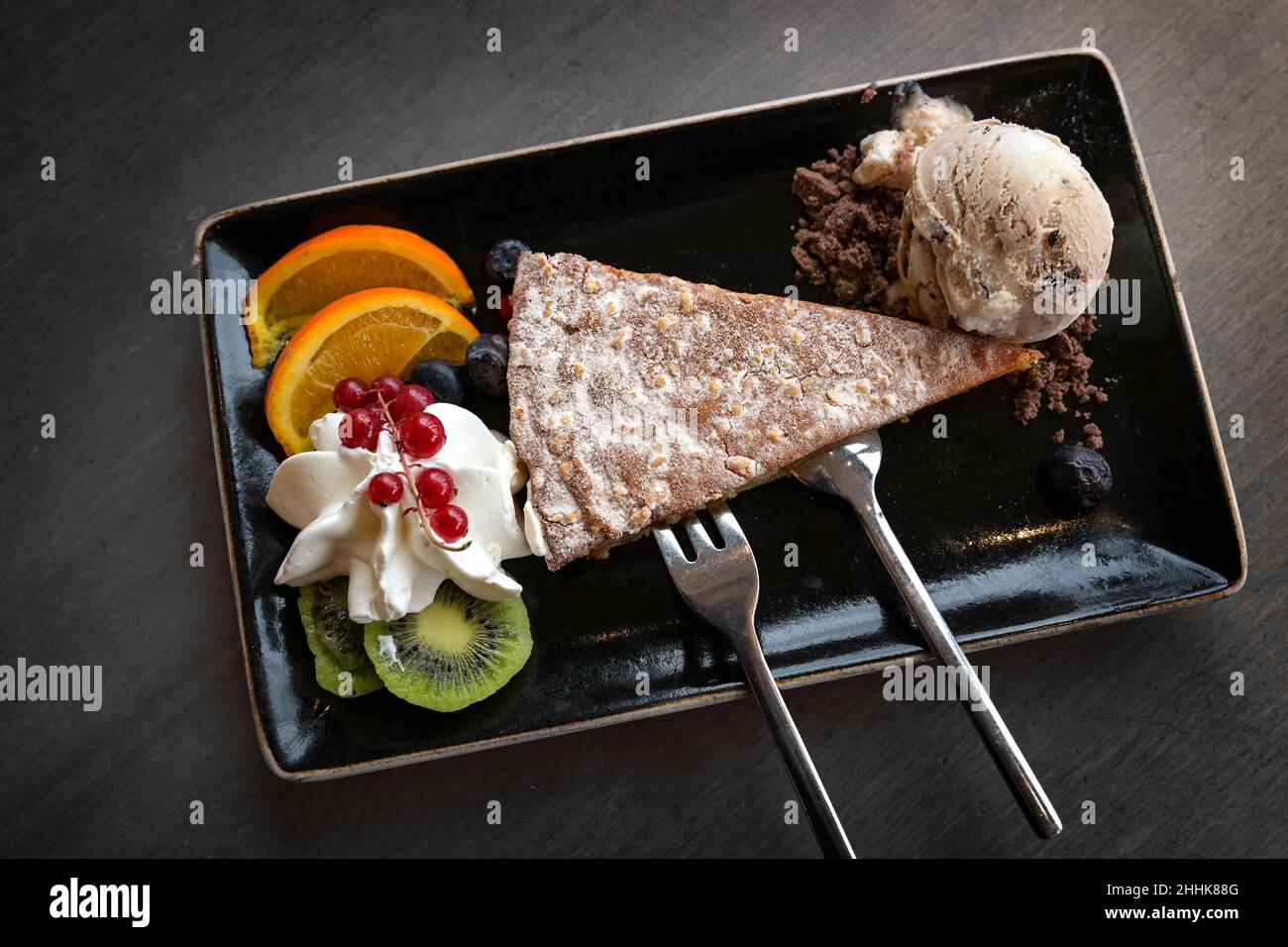 Gâteau aux amandes avec glace et fruits sur une assiette noire et une table gris foncé, délicieux dessert, vue d'en haut Banque D'Images