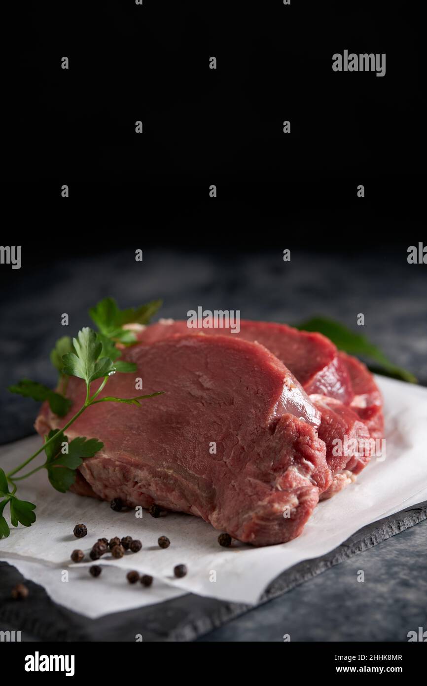 Du dessus du filet de bœuf frais non cuit avec du persil vert placé sur une plaque d'ardoise avec du papier parchemin dans la cuisine Banque D'Images