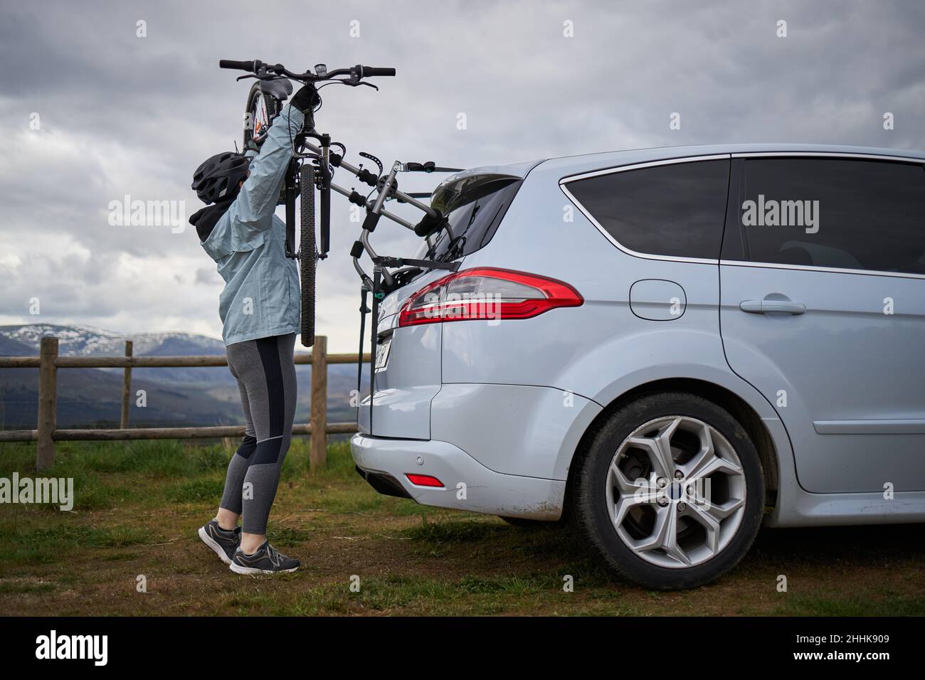 Vue latérale de la carrosserie d'une personne sportive méconnue dans un casque qui prend le vélo du porte-coffre d'une voiture garée à la campagne Banque D'Images
