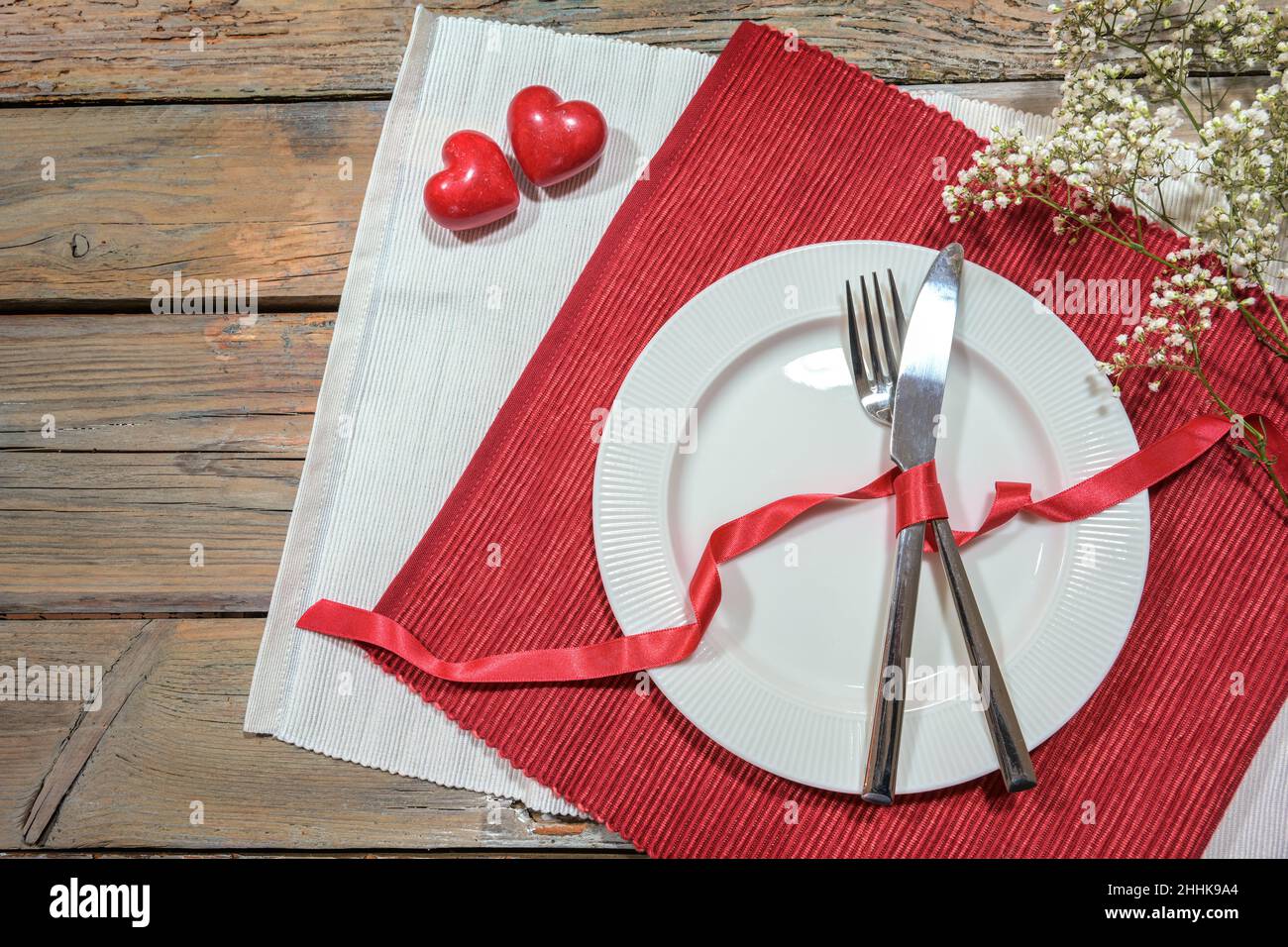 Table pour un dîner romantique avec deux coeurs, plat et couverts sur des serviettes rouges et blanches, concept amour, table rustique en bois avec espace copie, hig Banque D'Images