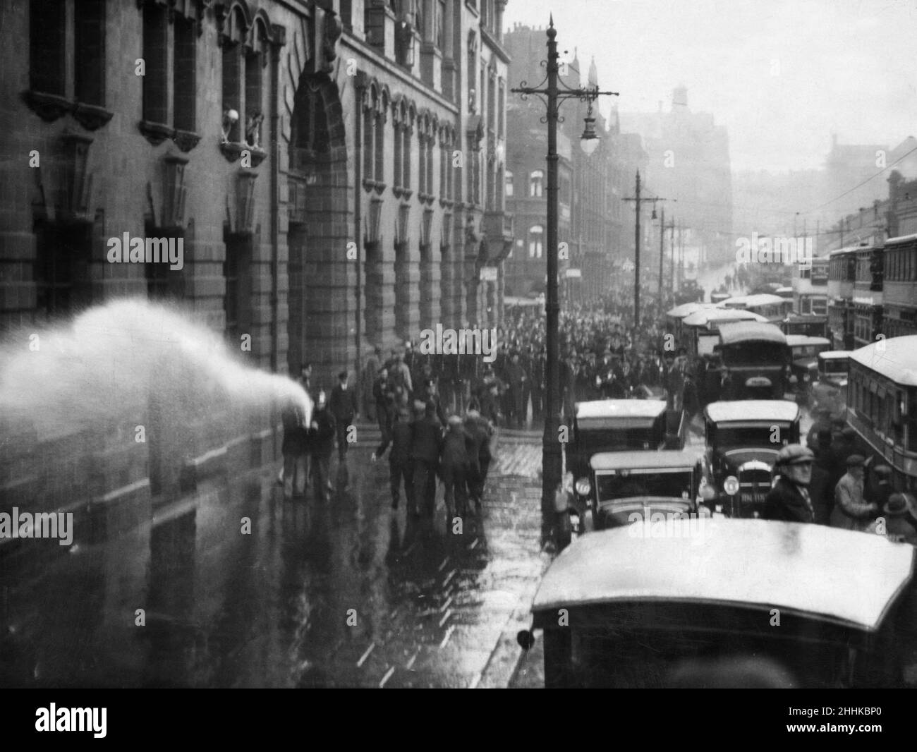 Une scène de chaos et de confusion pendant que les pompiers tournent le tuyau sur une démonstration de chômeurs des travailleurs organisés par le mouvement national des chômeurs (NUWM) à la jonction de Fairfield Street Manchester.La marche a été une protestation contre les réductions des allocations de chômage, de soins de santé, de maternité et de protection de l'enfance imposées aux chômeurs.Ils ont défilé sur Ashton Old Road depuis Openshaw, mais quand ils ont atteint la jonction de Downing Street et Fairfield Street, une rangée de policiers montés ont barré le chemin.Derrière les chevaux se trouvait une double rangée de la police des pieds et derrière eux une barricade Banque D'Images