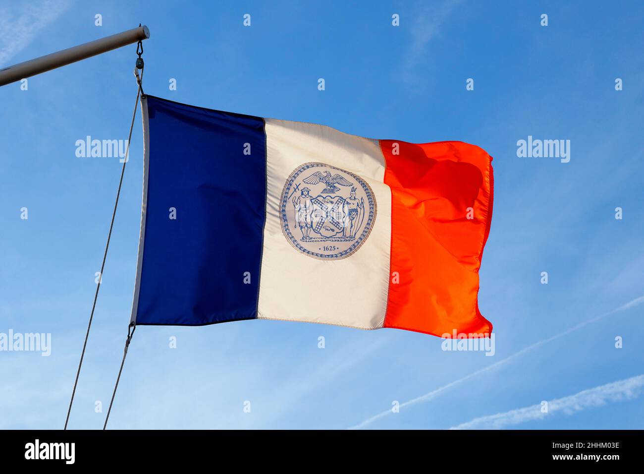 Un drapeau tricolore rétroéclairé et lumineux de la ville de New York volant sur un bras de yard avec un ciel ensoleillé. Banque D'Images