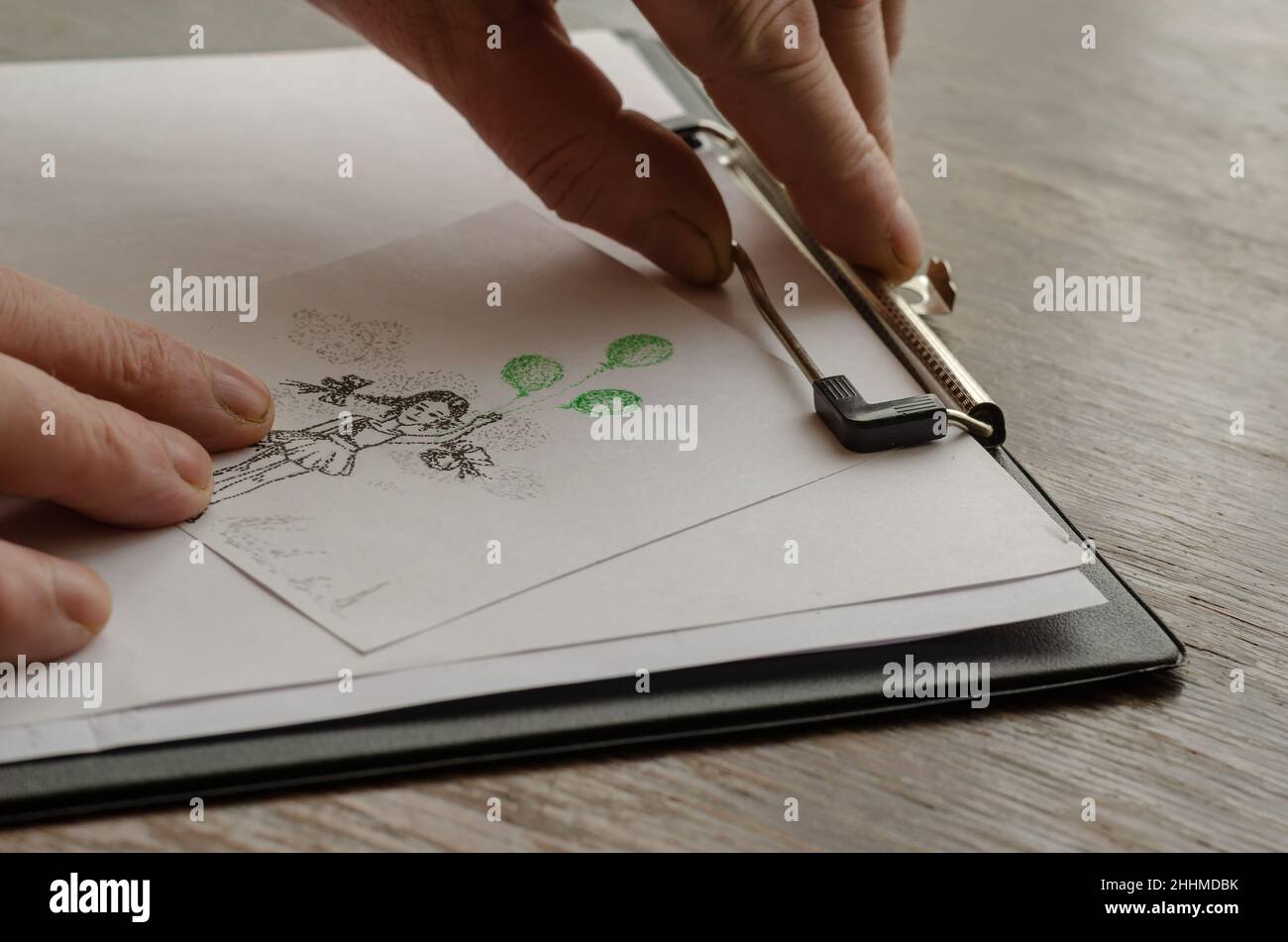 Les mains de l'homme appuient une feuille de papier avec un dessin dessiné à la main contre une tablette.Technique de dessin au stylo en pointillés.Dessin de fille avec des ballons verts sur papier Banque D'Images