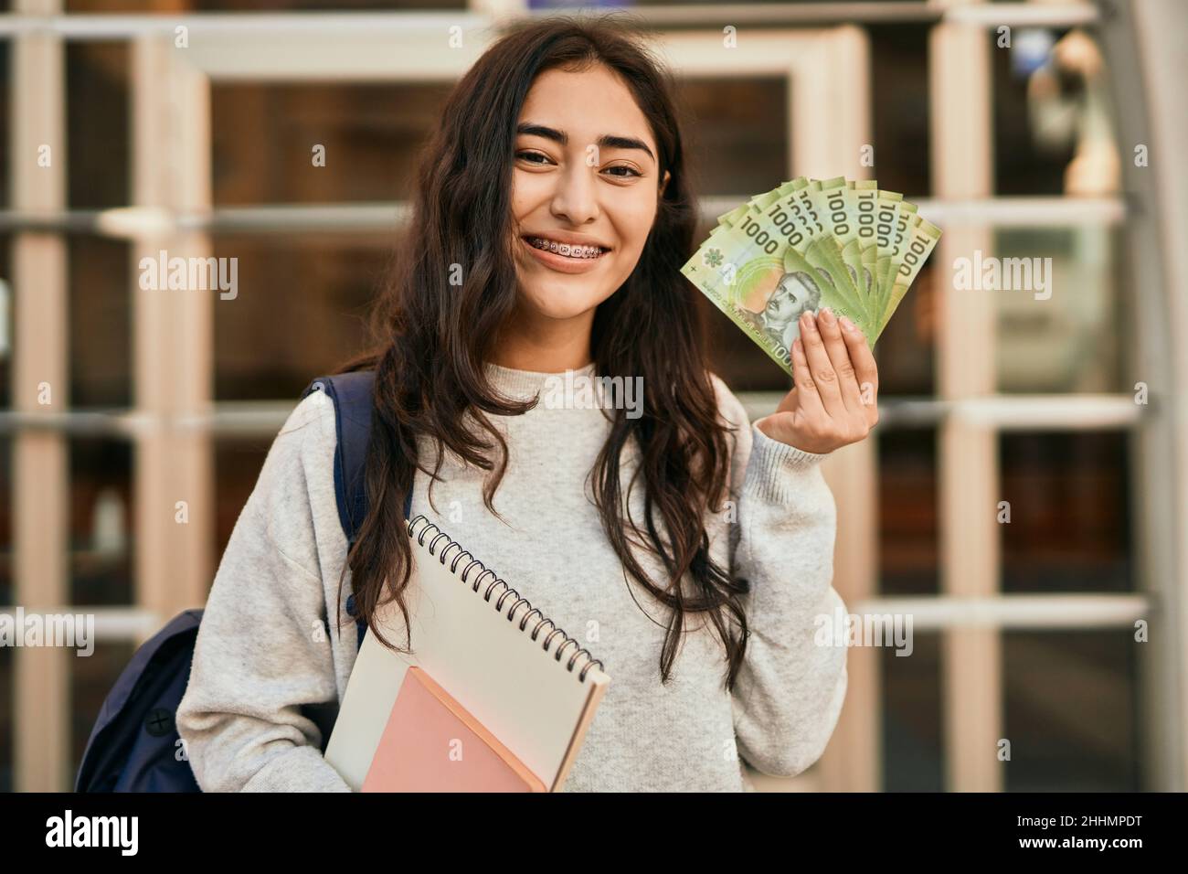 Une jeune fille étudiante du Moyen-Orient souriante et heureuse tient des billets de banque chiliens en pesos dans la ville. Banque D'Images