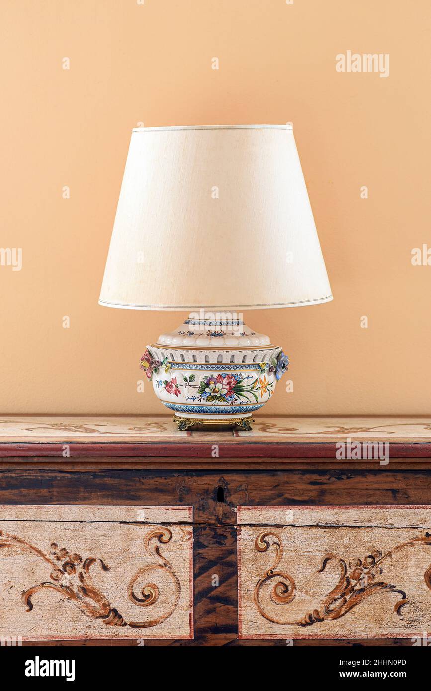Lampe à l'ancienne avec abat-jour léger placé sur une armoire en bois ornementale contre un mur beige Banque D'Images