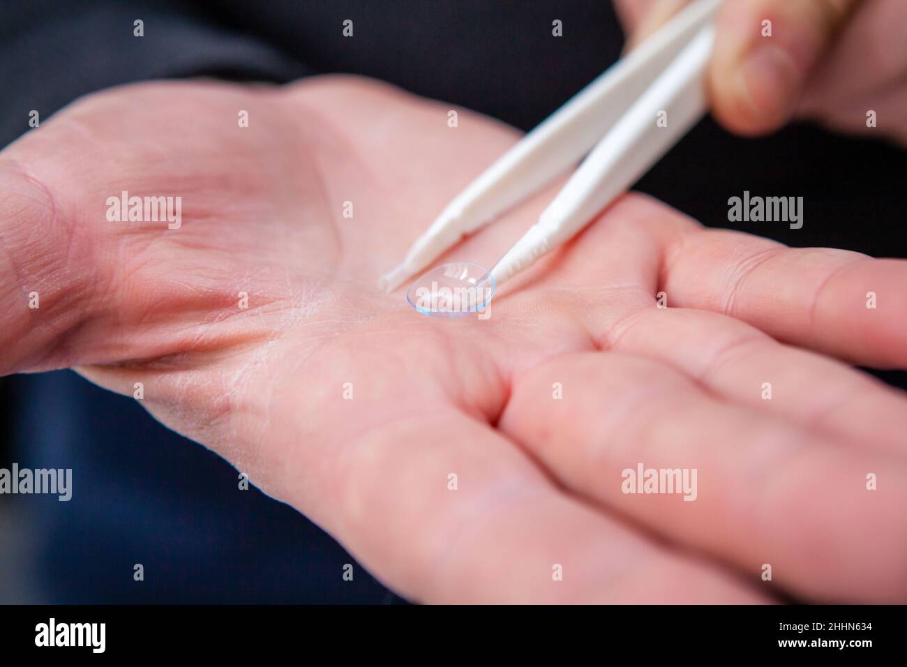 Un opticien masculin montre une lentille de contact claire et propre reposant sur la paume de sa main à l'aide d'une pince à épiler Banque D'Images