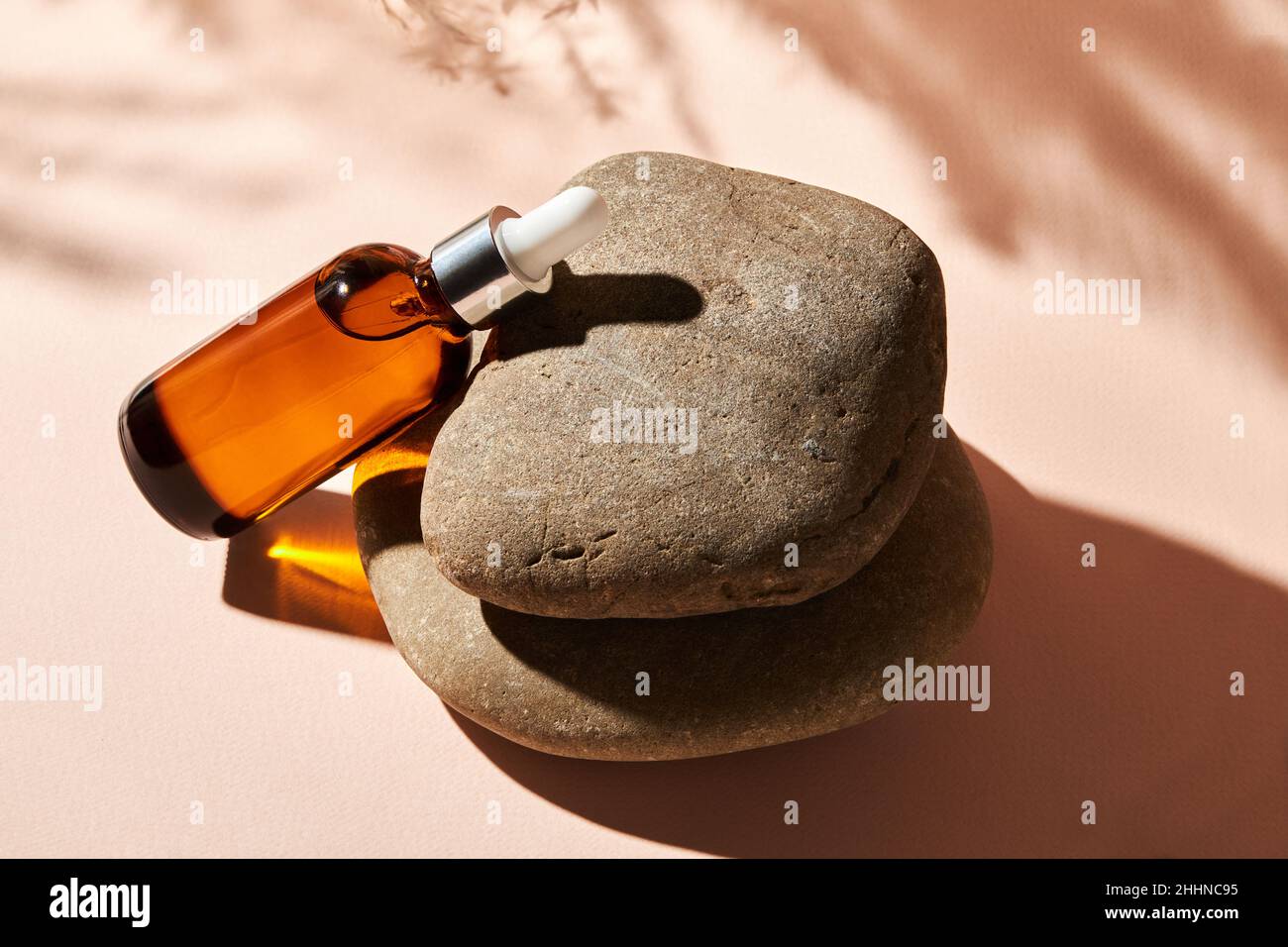 Huile essentielle sur une pierre de galet de rivière sur un fond beige.Produit de beauté médical cosmétique en bouteille de verre brun avec une pipette pour l'aromathérapie, al Banque D'Images