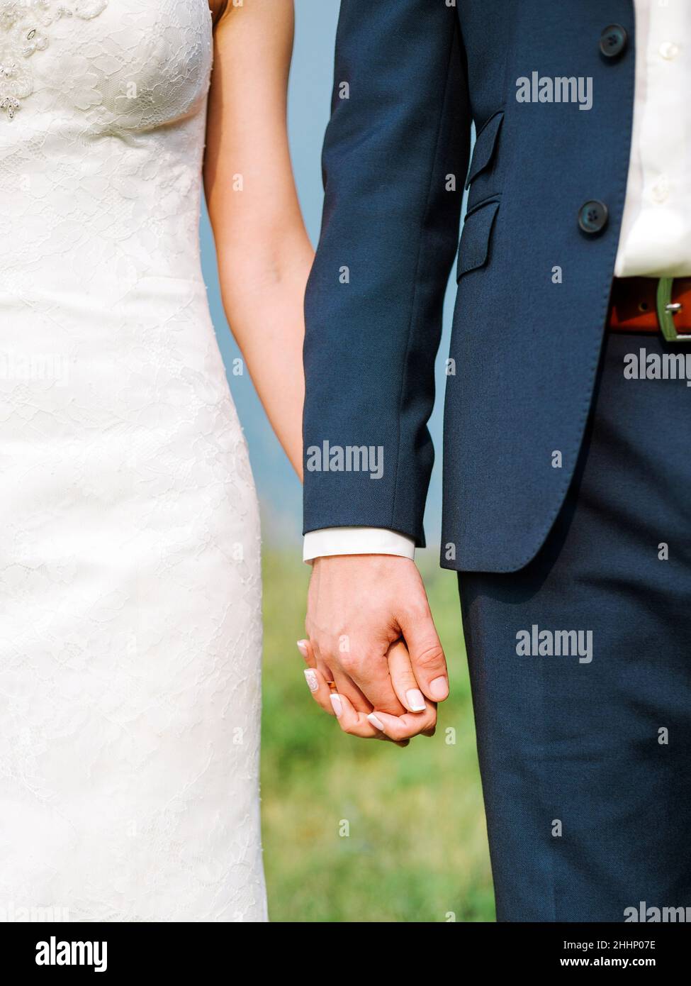 Vue rapprochée d'un couple marié tenant la main lors d'une cérémonie de mariage en plein air.Mariée en dentelle blanche robe de mariage et marié en costume bleu debout ensemble o Banque D'Images