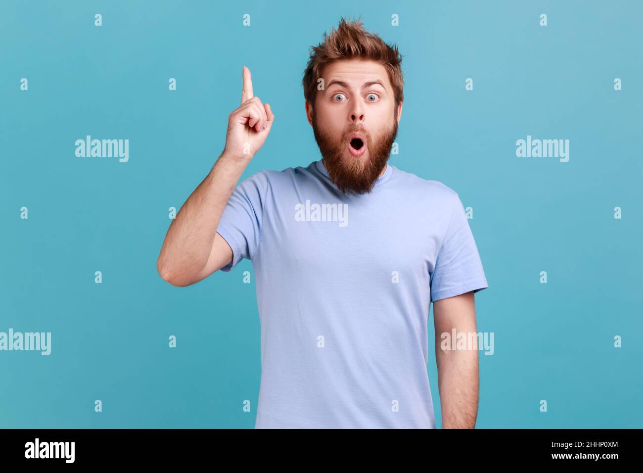 Eureka.Portrait de l'homme barbu souriant intelligent pointant du doigt vers le haut, a une bonne idée génie plan, inspiration et créativité, garde la bouche ouverte.Studio d'intérieur isolé sur fond bleu. Banque D'Images