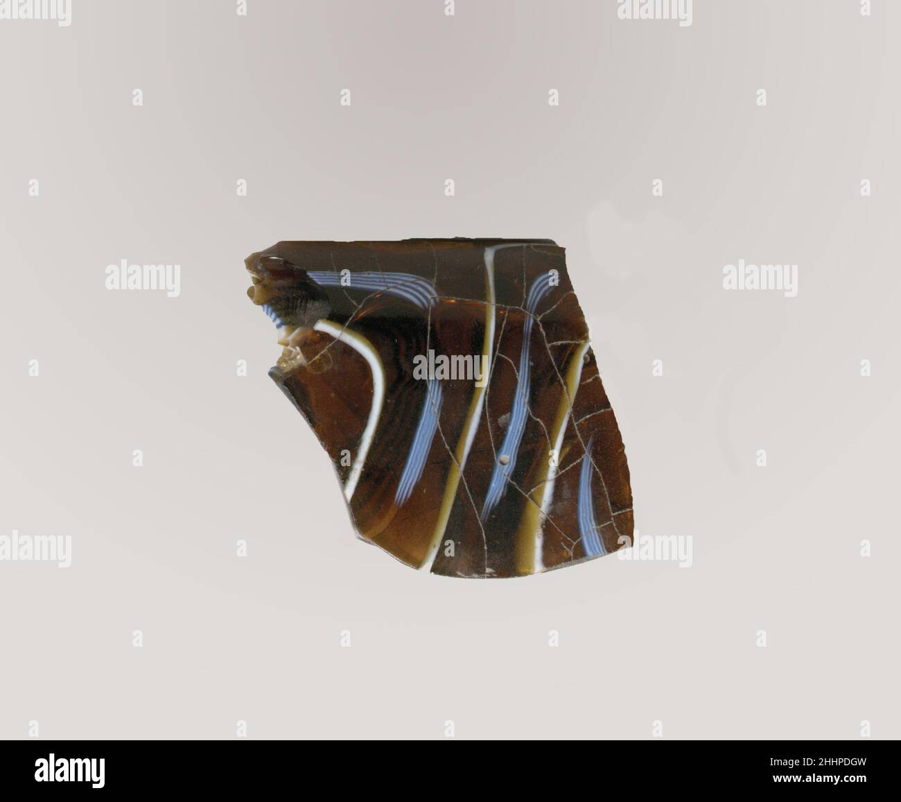 Fragment de bol nervuré en mosaïque de verre fin du 1st siècle C.-B.–début du 1st siècle A.D. fragment de Rim romain.brun miel foncé translucide, bleu cobalt et blanc opaque.rebord en saillie avec bord épais et arrondi; côté droit en dépouille vers le bas;Indentations irrégulières de l'outillage sur le col entre le rebord et la nervure sur le corps.motif en mosaïque spiralée formé de sections d'une canne simple au sol brun avec des fils blancs et bleus en lignes horizontales parallèles; à l'extérieur, une nervure verticale avec dessus aplati et bord extérieur arrondi.intérieur poli;piqûres de bulles de surface et de fissures à l'intérieur ; morcellement, faible altération, et Banque D'Images