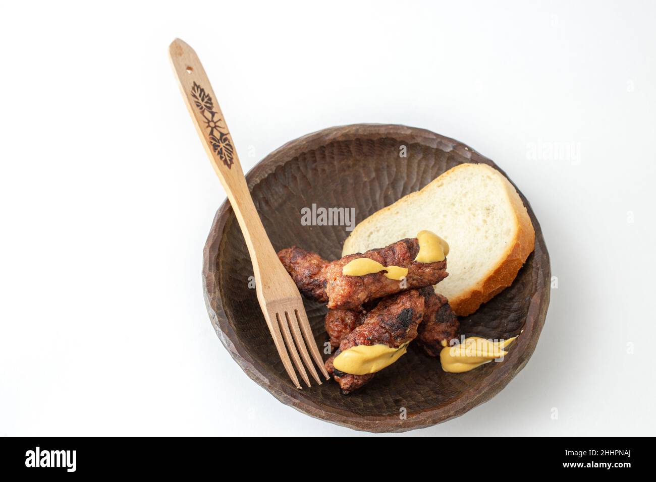 Roulés de viande hachés roumains, mici ou mititei sur un bol en bois sculpté avec de la moutarde et une fourchette traditionnelle en bois, isolée sur fond blanc Banque D'Images