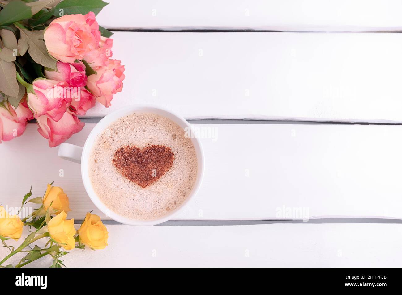 Vue de dessus d'une tasse à café en forme de coeur cannelle et de belles roses sur table en bois blanc, espace copie Banque D'Images