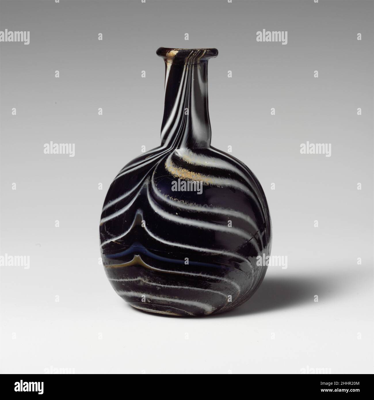 Flacon de parfum en mosaïque de verre 1st moitié du 1st siècle A.D. Roman Translucent bleu de cobalt profond, avec des traces translucides brun miel, blanc opaque, bleu clair opaque et jaune opaque.rebord arrondi éverté; col cylindrique, se développant légèrement vers le bas, avec un retrait fin autour de la base; corps globulaire;Fond concave. Motif en mosaïque rayé de pistes appliquées enroulées autour d'un sol bleu, puis outillées en quatre coups, alternant vers le haut et vers le bas, en un large motif en plumes. Cassé et réparé, avec une grande puce dans le rebord, et un trou et quelques petites fissures dans le corps; quelques grosses bulles; de légères irides Banque D'Images