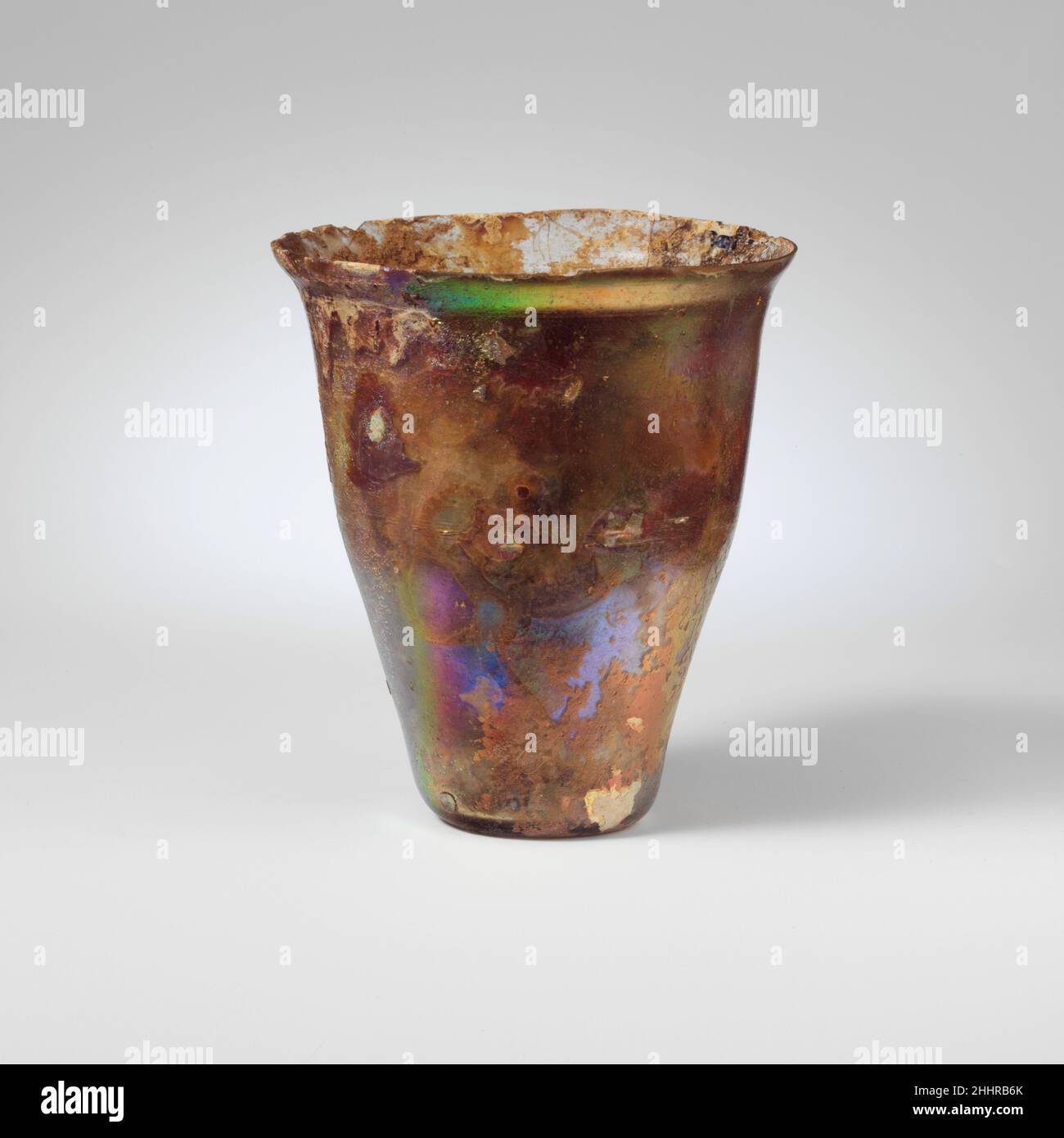 Bécher en verre 1st Century A.D. Roman incolore. Rebord rodé; collier légèrement bombant sous le bord; côtés sculptés vers le bas; fond concave. Une fine ligne horizontale de découpe à la roue sous le collier de 3/8 po.(9 mm) sous la jante), deux bandes plus larges de 1/16 po(1,5 mm) plus loin vers le bas du corps, juste au-dessus du tour, 1 5/8 po(41 mm) sous le rebord. Presque complet sauf pour les petites copeaux abîmés dans le rebord et les fissures autour du rebord; piqûres et bulles plus grandes; piqûres profondes, iridescence brillante et altération crémeuse; altération semblable à l'émail noir et accrétion du sol à l'intérieur.Bécher en verre 239813 Banque D'Images