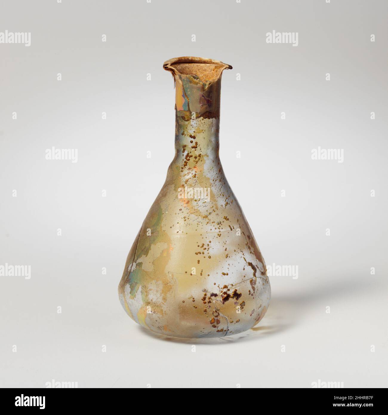 Flacon de parfum en verre 1st Century A.D. Roman incolore avec teinte bleu pâle vert. Rebord replié, sur, et dans; légèrement en forme d'entonnoir, col cylindrique,Avec de faibles repères d'outillage autour de la base ; corps piriforme ; fond plat.deux crêtes grossièrement horizontales (sentiers marrés ?)Autour du haut du corps.cassé et réparé; la moitié de la jante est manquante; trois trous dans le corps et le fond, et de nombreuses fissures; de nombreuses petites bulles et piqûres; des intempéries en mosaïque et irisées; des taches de vieillissement épais, semblable à de l'émail restant sur la jante et le haut du cou.Verre très fin, extrêmement abîmé.Flacon de parfum en verre 239783 Banque D'Images