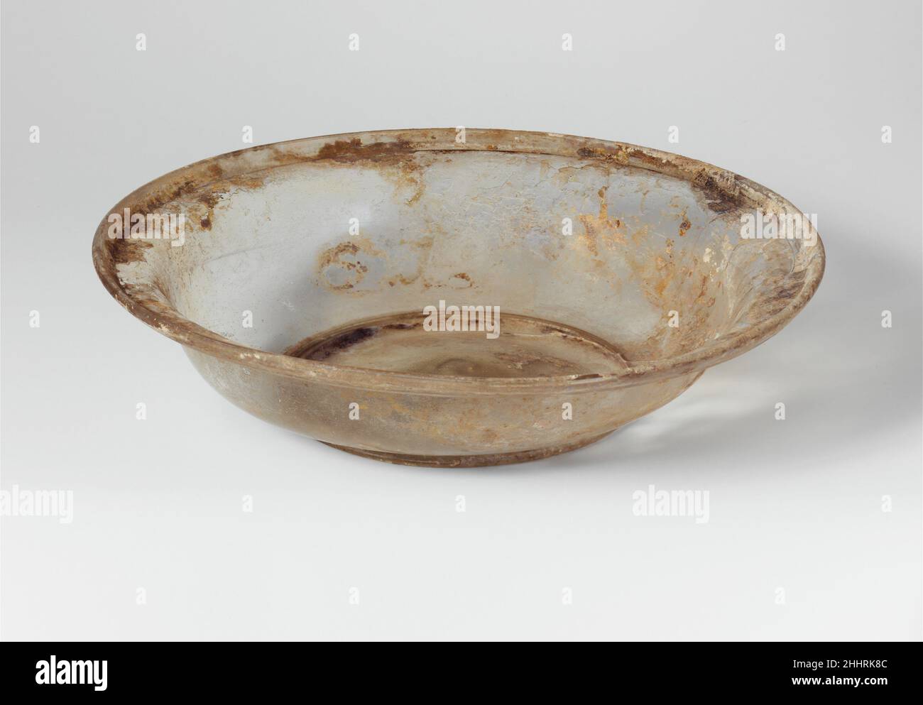 Boîte en verre 4th Century A.D. Roman incolore avec une teinte jaune pâle vert. Tubulaire, rebord évasé, plié vers l'extérieur et vers le bas, avec une épaule interne presque horizontale ; en S d'un côté à l'autre du corps, courbé vers l'anneau de base tubulaire intégral ;Un fond légèrement concave, légèrement boiteux au centre avec une petite cicatrice de pontil. Cassé et réparé, fissuré d'un côté et un grand trou de l'autre; des bulles pinçantes; des piqûres, des intempéries irisées et un peu de limie enchâssée autour de la jante.Plat en verre 239890 Banque D'Images