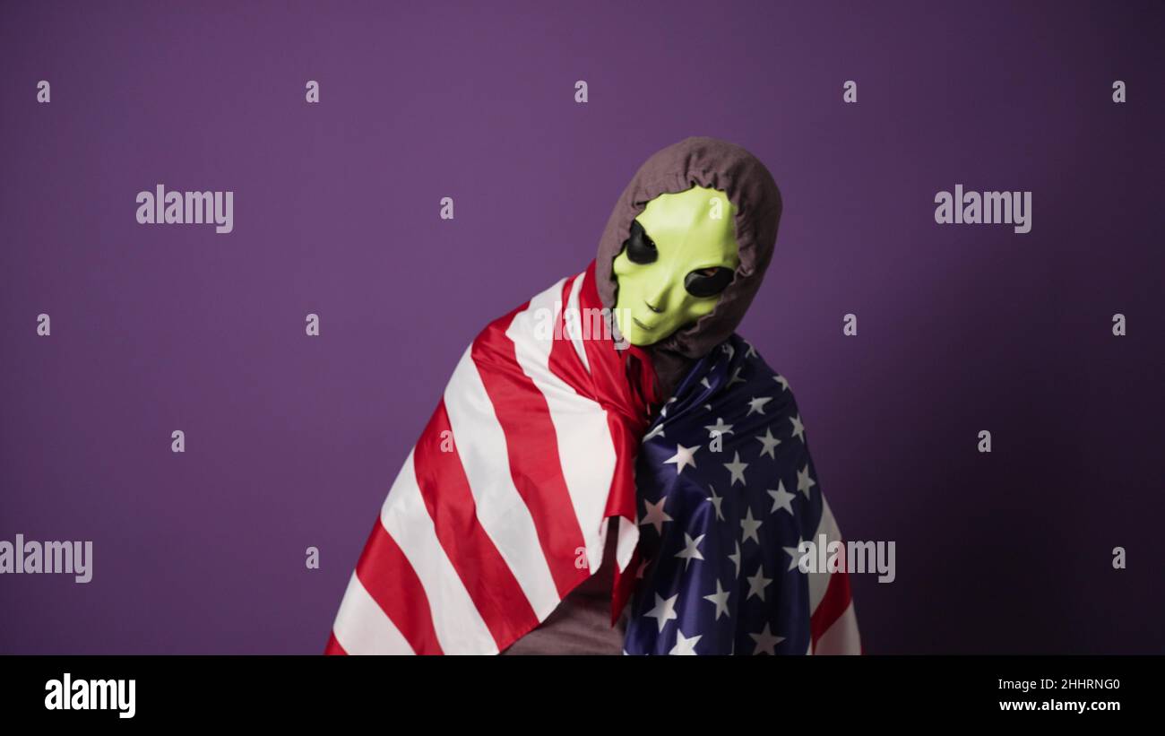 Alien porte un pull à capuche violet avec des lacets de capuche attaché  sous les mentonnières enveloppés d'un drapeau américain dans une ambiance  heureuse sur fond violet gros plan Photo Stock -