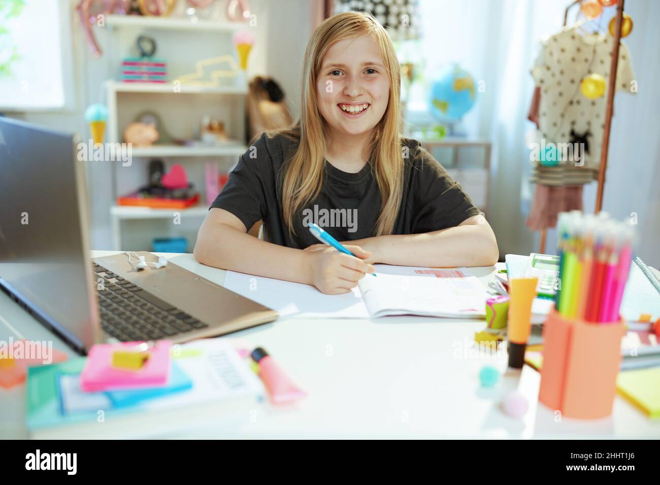 souriant moderne fille en chemise grise avec ordinateur portable et cahier d'exercices ayant l'éducation en ligne à la maison dans le soleil jour. Banque D'Images