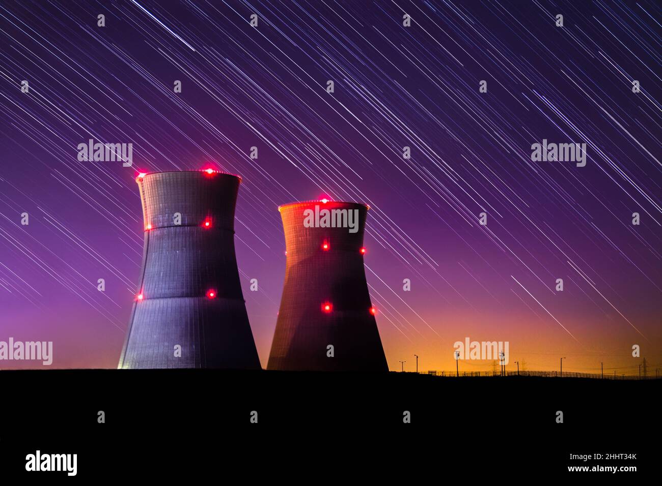 Une image astrophotographique d'une centrale nucléaire avec un coucher de soleil violet coloré et des pistes étoiles la nuit. Banque D'Images