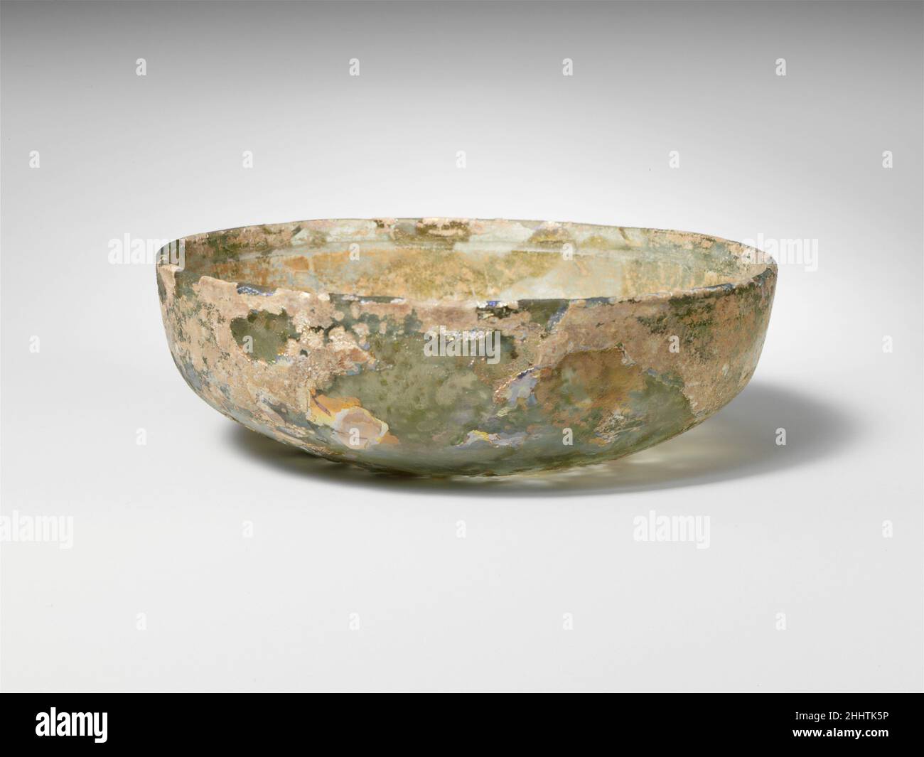 Bol en verre fin du 1st siècle C.-B.–début du 1st siècle A.D. Roman translucide bleu très pâle vert.vertical, rebord arrondi;Faces supérieures convexes, puis tournées en biais et courbées vers le bas jusqu'à fond plat.décoration intérieure découpée en forme de roue, comprenant une large rainure horizontale sous la jante et deux lignes parallèles plus étroites à l'angle dans les côtés.intactes, mais fissures internes et petites encoches dans la jante; peu de bulles;piqûres profondes, iridescence brillante et altération blanche laiteuse.Bol en verre 244701 Banque D'Images