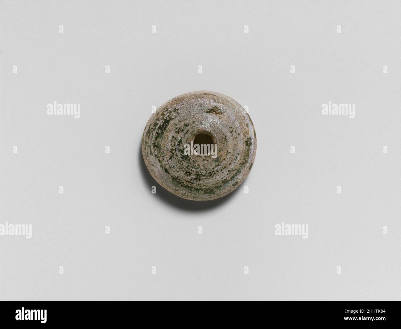 Broche en verre env.1st–3rd Century A.D. Roman translucide bleu pâle vert.bord supérieur rugueux autour du trou; corps bombé; fond plat; trou vertical plus grand sur le fond.fissures intactes mais internes; cicatrice d'outillage sur la surface supérieure bombée; altération bleutée et irisée.réalisée par chemin de bobinage dans une spirale autour de la tige.Broche en verre whor 244745 Banque D'Images