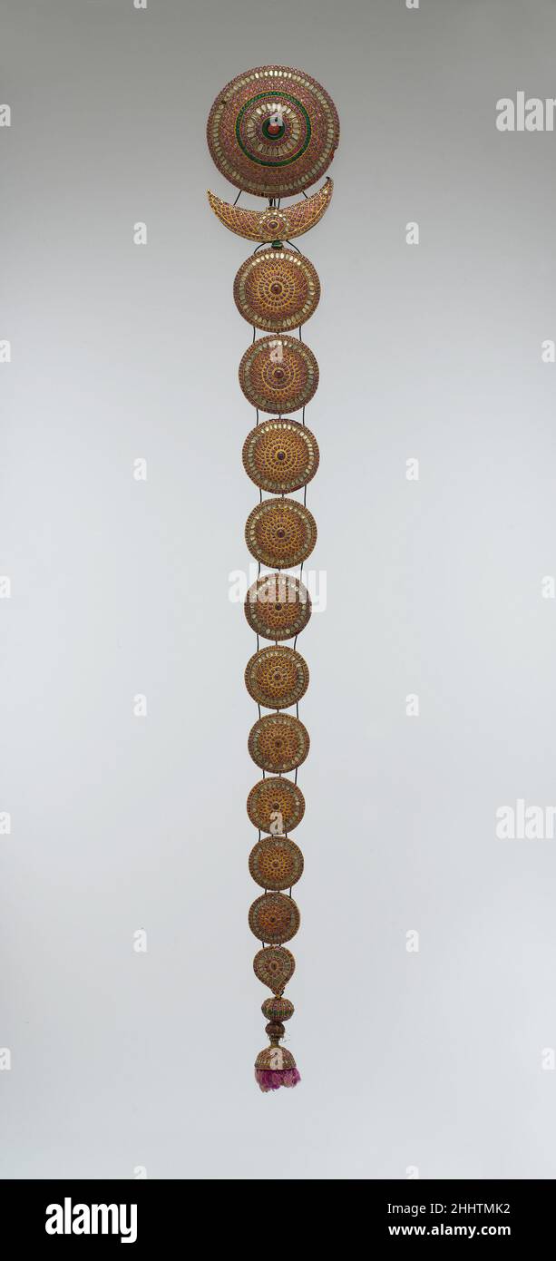 Ornement de tresse (Jadanagam) 18th–19th siècle ce type d'ornement de tresse, généralement porté par des épouses et des danseurs, est appelé jadanagam (serpent à cheveux) pour le regroupement de serpents peut avoir été attaché à son disque le plus haut.Ce disque et la forme du croissant ci-dessous représentent le soleil et la lune.Décoré dans la technique de kundan dans laquelle des centaines de rubis, émeraudes, améthystes, et morceaux de cristal de roche ont été incrustés dans la feuille d'or malléable et fait affleurant avec la surface de l'ornement, l'objet entier aurait étincelé avec le mouvement de son porteur.Dans la tradition hindoue, la bravoure d’une femme Banque D'Images