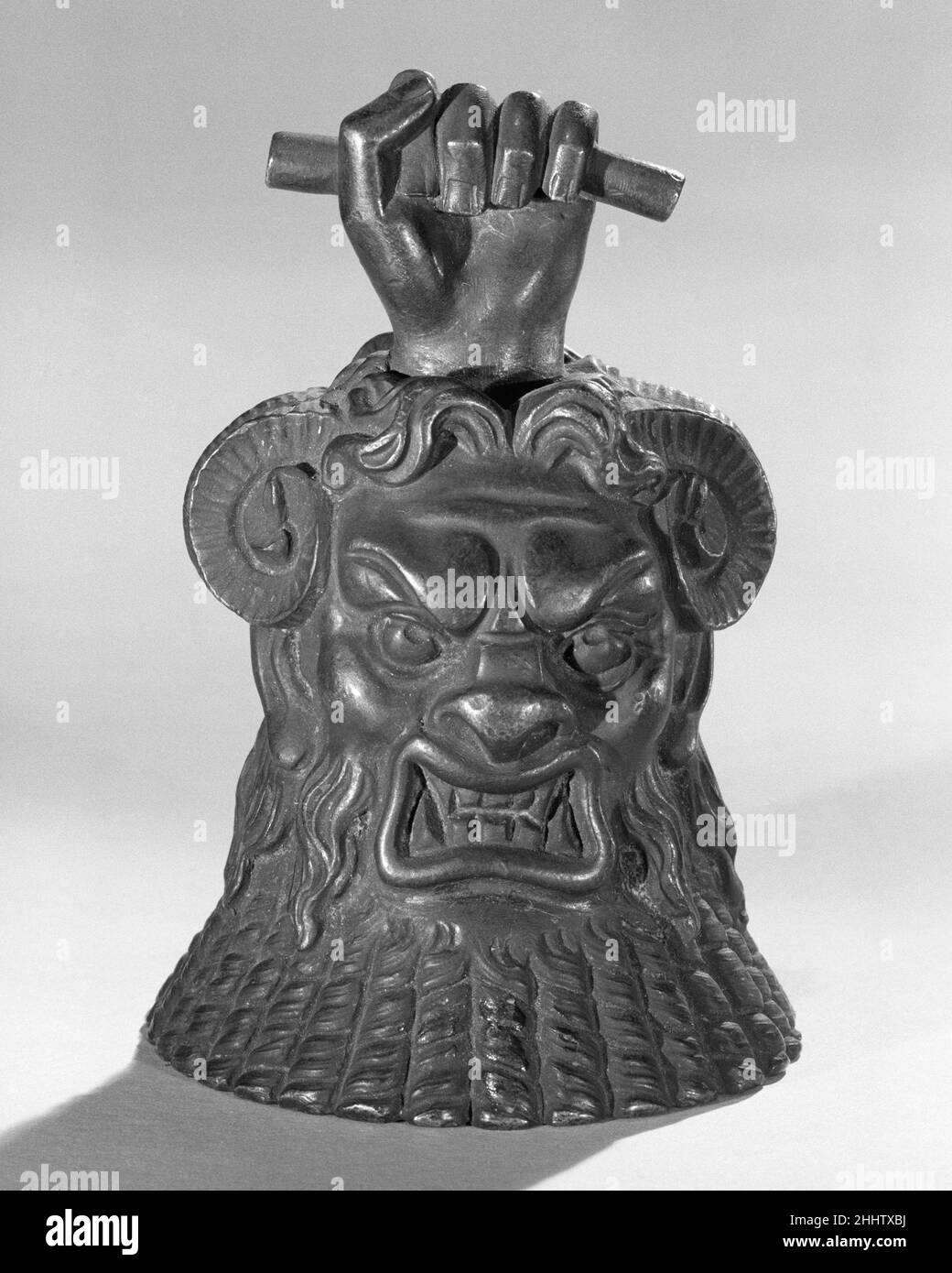 Main Bell 19th siècle européen au 19th siècle, l'intérêt pour l'Égypte ancienne a balayé l'Europe après les campagnes de Napoléon (1798-1801).Cette cloche clapper très stylisée présente le visage de la divinité égyptienne BES, ainsi que des attributs qui ne lui sont normalement pas associés, y compris les cornes de béliers et le 'Wand of Horus' (le poing saisit une petite tige).Sonnerie manuelle.Européen.19th century. métal.Idiophone-frappé-cloche-clapper Banque D'Images