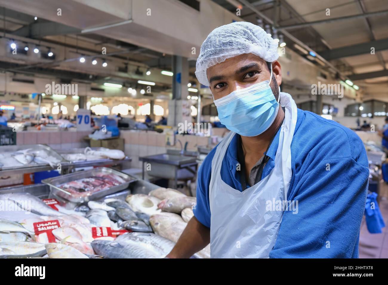 Attention sélective au visage sympathique joyeux de jeune adulte beau Moyen-Orient masque de poisson, vendre du poisson frais sur le marché traditionnel du poisson. Banque D'Images