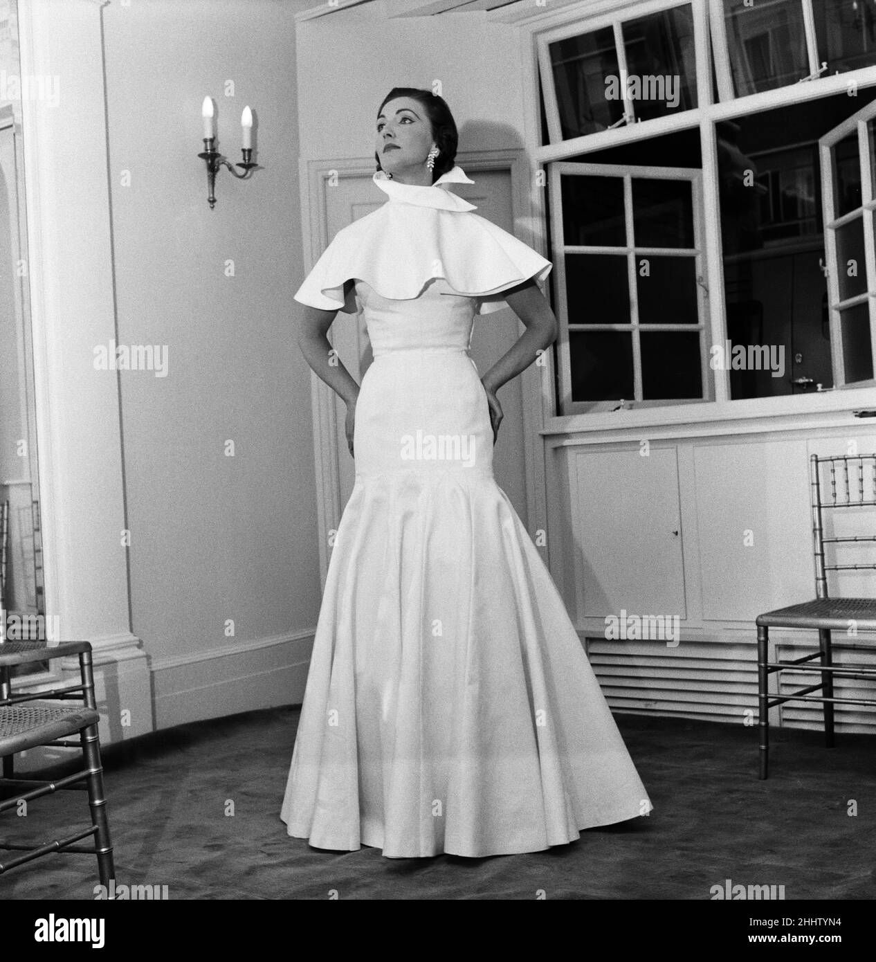Mode de Lachasse Ltd. 'Diesree' Une robe de soirée ajustée en coton blanc épais pique.L'énorme jupe s'épare du genou et il y a une petite cape assortie avec un col montant.Juillet 1955. Banque D'Images