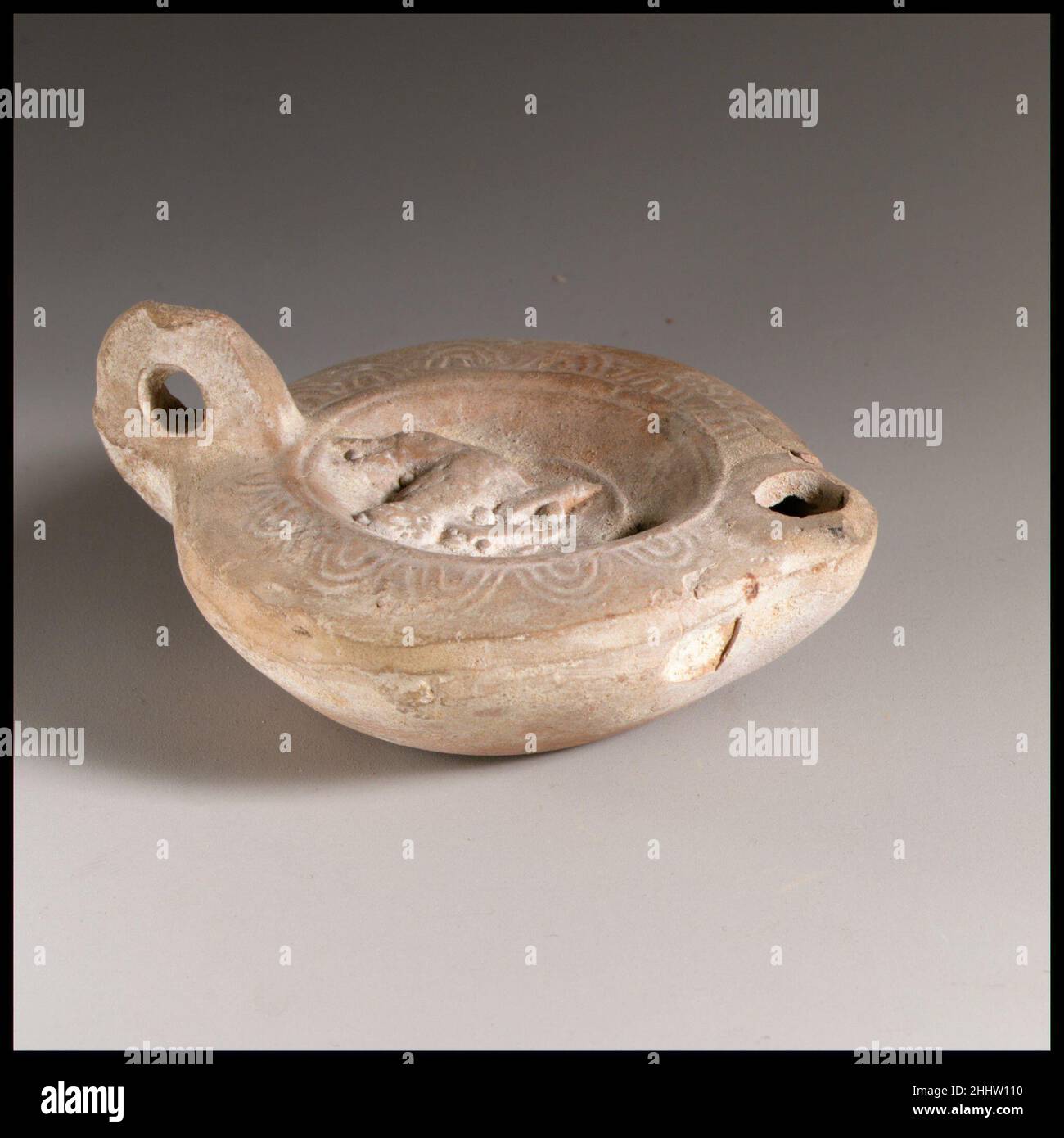 Lampe à huile en terre cuite 2nd Century A.D. Roman Loeschcke Type 8.Moulé, avec poignée percée.Discus concave: Oiseau en relief élevé vers la droite mais tête tournée vers la gauche, tenant une baie (?)dans son bec; d'autres baies à ses pieds; derrière, un cercle surélevé; un seul trou de remplissage,près du centre inférieur ; bande d'une rainure et ligne autour de l'arête.Épaule légèrement inclinée : grandes ovules impressionnées, chacune comprenant deux lignes cintrées et une langue centrale.Grande poignée non décorée.Brosse en forme de cœur.Base large, non définie et légèrement concave. Intacte.Lampe à l'huile en terre cuite.Romain.2nd siècle A.D..Terramaco Banque D'Images