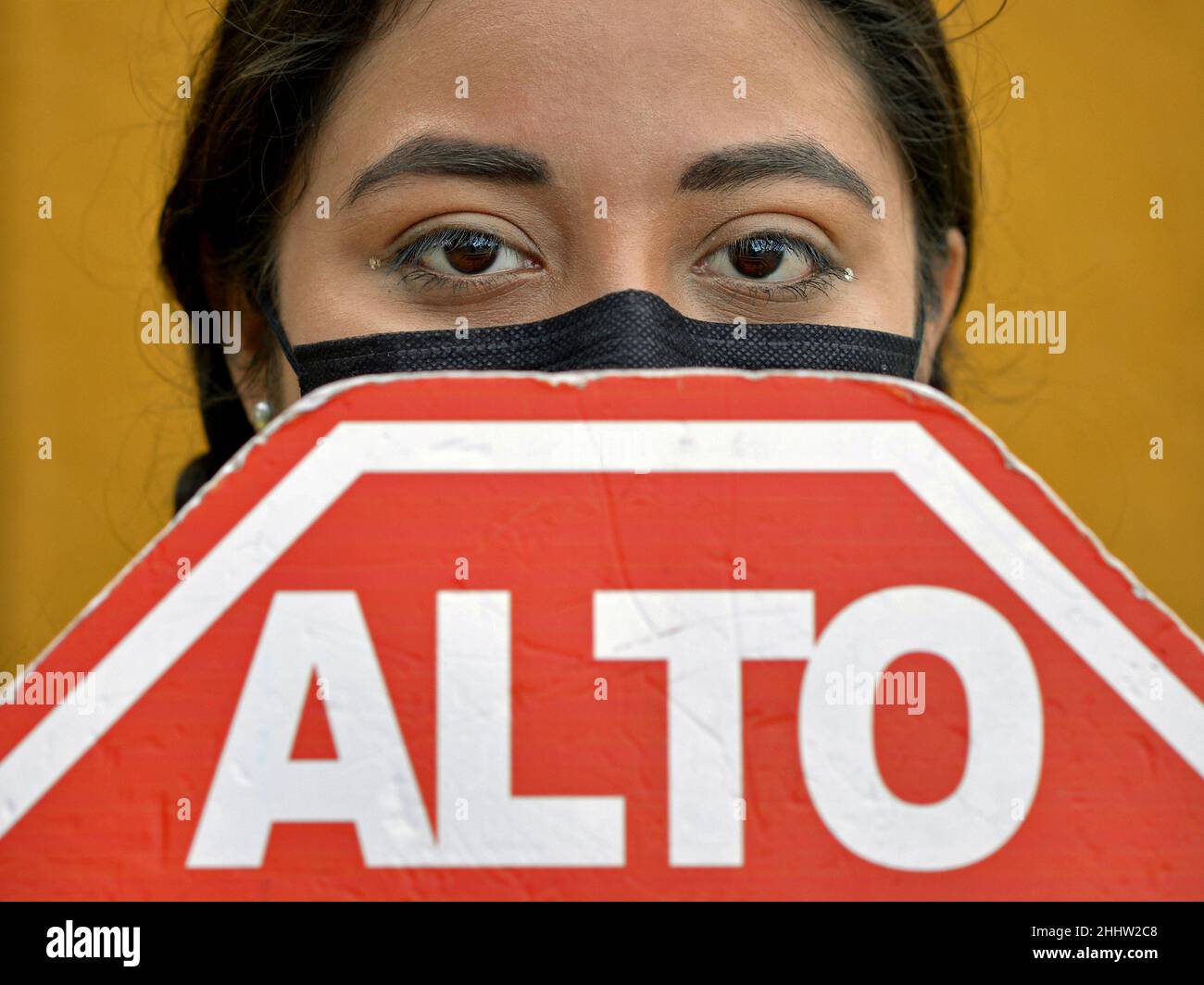 Une jeune femme mexicaine aux yeux bruns couvre son visage avec un masque facial noir jetable et un signe d'arrêt mexicain rouge pendant une pandémie de corona. Banque D'Images