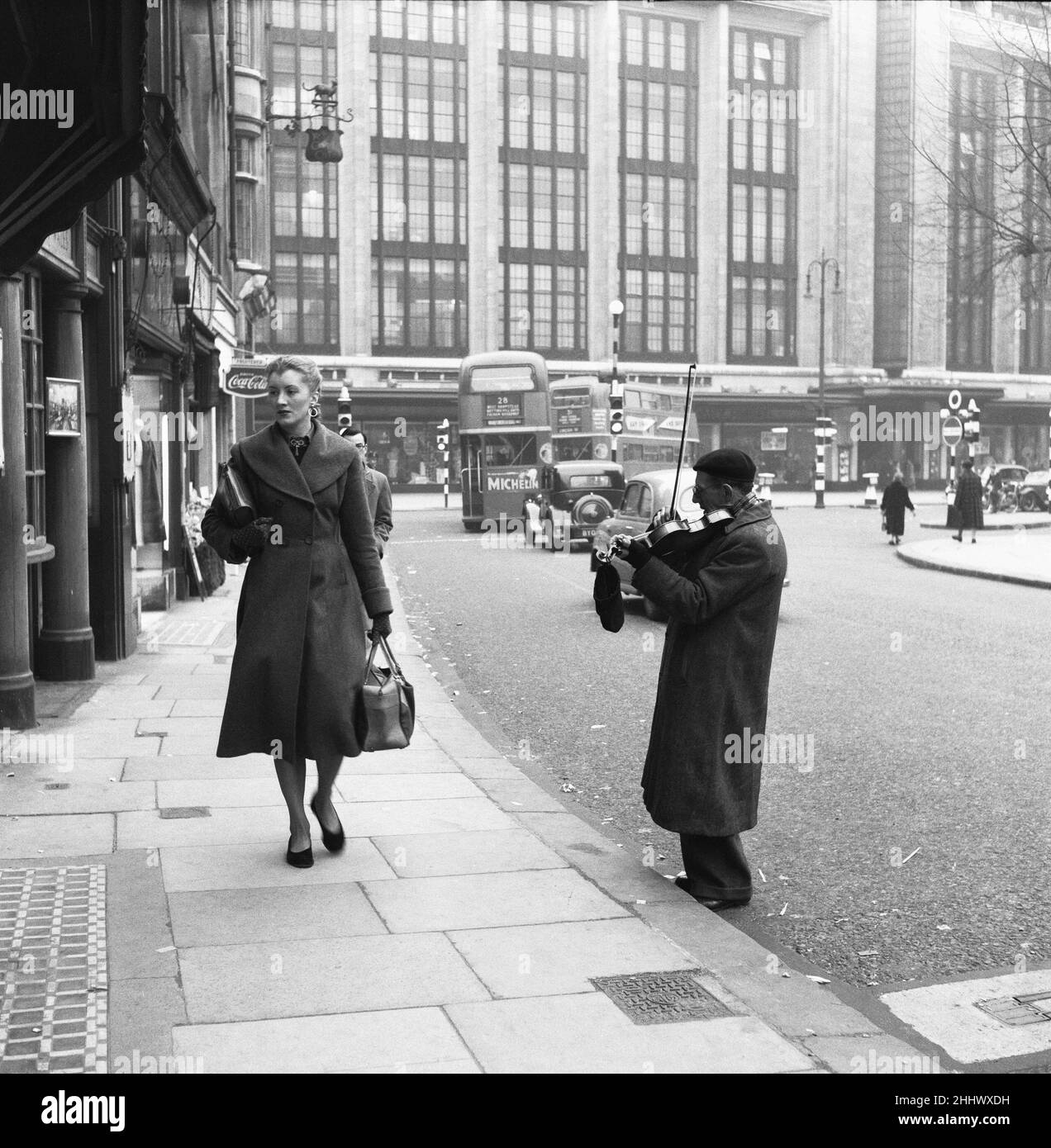 Un musicien de rue sérénade un acheteur de passage à Church Street, Kensington.17th mars 1954 Banque D'Images