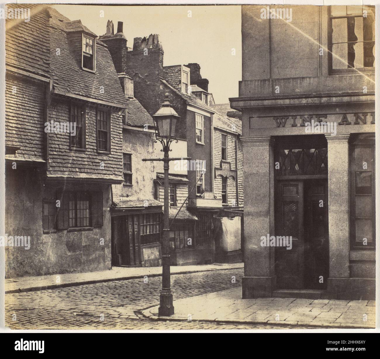 [Rue avec Lamp Post et Wine Shop] 1850s Inconnu en 1841 William Henry Fox Talbot a breveté le premier processus photographique négatif-positif, qui a formé la base de la photographie jusqu'à l'ère numérique.Le photographe a placé un morceau de papier couché dans une solution de sels d'argent photosensibles dans l'appareil photo, l'a exposé à la lumière du soleil et a développé l'image latente pour produire un négatif qui pourrait ensuite être imprimé comme plusieurs positifs.Toutes les imperfections du négatif ont été reproduites dans l'impression.Ici, le coin manquant du négatif a été éliminé par le recadrage.Un lampadaire à gaz moderne ancres TH Banque D'Images