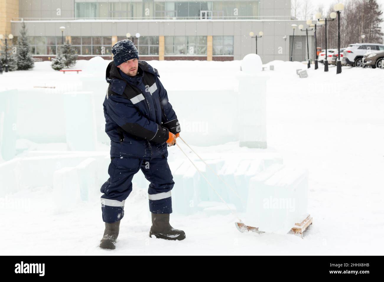 Un homme dans une veste bleue et un bonnet tricoté noir porte des panneaux de glace sur un traîneau en bois Banque D'Images